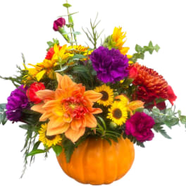 Mixed bouquet in an orange pumpkin container with bright yellow, orange, red, and purple flowers