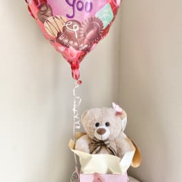 Heart-shaped balloon above a teddy bear in a pink gift box