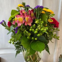 Mixed bouquet of pink, yellow, purple, and red flowers in a clear glass vase