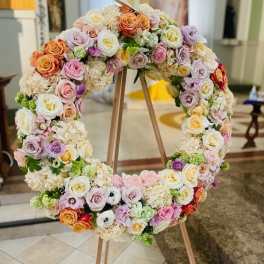 Large circular floral wreath on a wooden stand with pastel roses and hydrangeas
