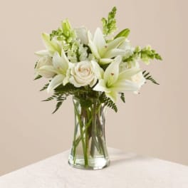 White lilies and a cream rose in a clear glass vase