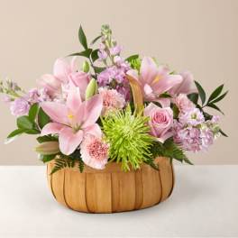 Pink lilies and roses arranged in a wooden basket with green accents