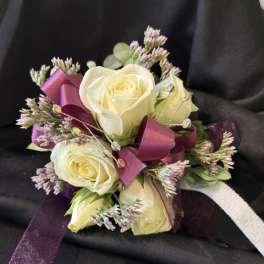 Small bouquet of cream roses with purple ribbon on black fabric