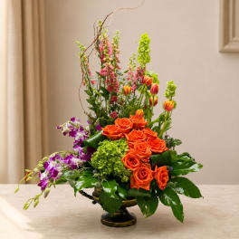 Orange roses and purple orchids in a low vase with tall pink blooms