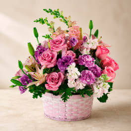 Pink and purple flower arrangement in a pink woven basket