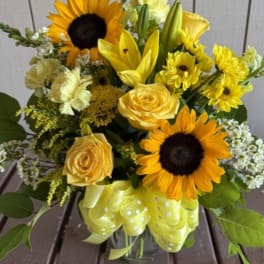 Yellow bouquet with sunflowers, roses, and lilies in a glass vase