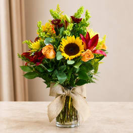 Mixed bouquet with sunflowers, roses, and lilies in a glass vase