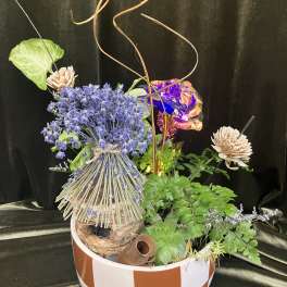 Mixed floral arrangement in a striped bowl with blue blooms and decorative accents