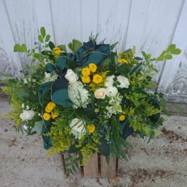 Large floral arrangement with white roses, yellow blooms, and dark green ribbon