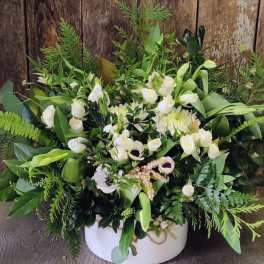 White floral arrangement in a round white box with lush greenery