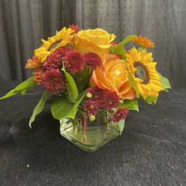 Sunflowers, yellow roses, and burgundy mums in a clear glass vase