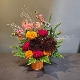 Mixed floral arrangement in a ribbed orange pot with pink, yellow, and dark blooms