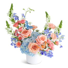 Peach roses and blue hydrangeas in a white vase with butterfly picks