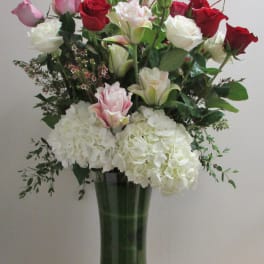 Tall bouquet of red, pink, and white roses with white hydrangeas in a glass vase
