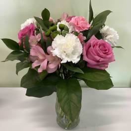 Mixed bouquet of pink roses, carnations, alstroemeria, and white blooms in a clear glass vase