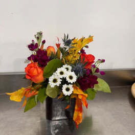 Mixed bouquet with orange roses, white daisies, and purple flowers in a black vase