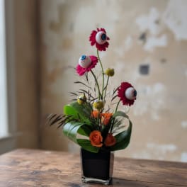 Small floral arrangement with orange roses and pink daisy-like blooms in a black vase