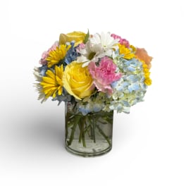 Mixed bouquet of yellow roses, daisies, and blue hydrangeas in a glass vase