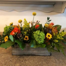 Low floral arrangement with orange roses, yellow blooms, and green hydrangea in a wooden box