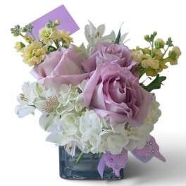 Lavender roses and white flowers in a square glass vase