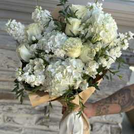 White rose and hydrangea bouquet wrapped in tan paper with a white ribbon