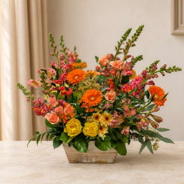 Mixed bouquet of orange, pink, and yellow flowers in a wooden container