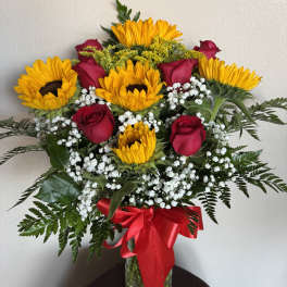 Sunflowers and red roses in a glass vase with a red ribbon