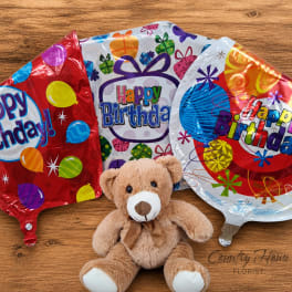 Teddy bear with three birthday balloons on a wooden surface