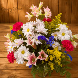 Mixed bouquet of daisies, lilies, carnations, and yellow filler in a glass vase
