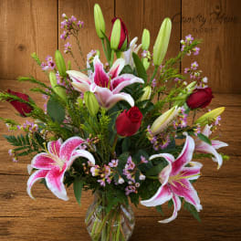 Bouquet of pink lilies and red roses in a clear glass vase