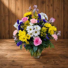 Mixed bouquet of pink roses, white daisies, and yellow blooms in a glass vase