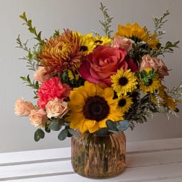 Mixed bouquet with sunflowers, roses, and mums in a ribbed glass vase
