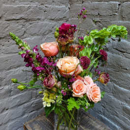 Mixed bouquet of peach roses and purple flowers in a clear glass vase