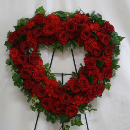 Heart-shaped wreath of red roses with green foliage on a stand