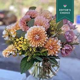 Peach dahlias and yellow filler flowers arranged in a clear glass vase
