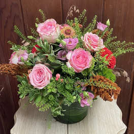 Mixed arrangement of pink roses and purple blooms in a leaf-wrapped glass vase