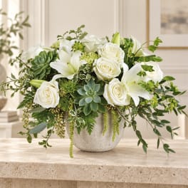 White roses and lilies arranged in a gray vase with green succulents