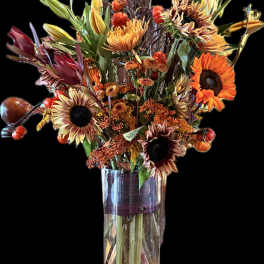 Autumn bouquet with sunflowers and orange blooms in a clear glass vase