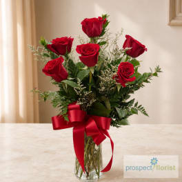 Red roses in a clear glass vase with a red ribbon bow