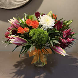 Mixed bouquet of orange roses, white chrysanthemum, and pink lilies in a glass vase