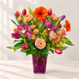Colorful mixed bouquet in a purple glass vase with tulips, orchids, and gerbera daisies