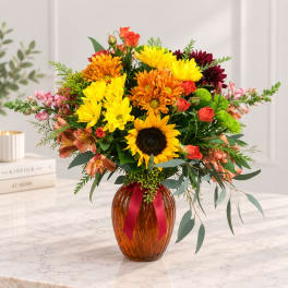 Mixed bouquet of sunflowers, daisies, roses, and orange blooms in an amber vase