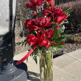 Red roses and chrysanthemums in a clear glass vase with a red ribbon