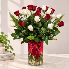Red and white roses in a clear glass vase with a red ribbon