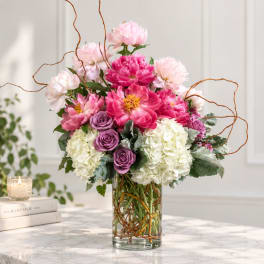 Pink and white floral arrangement in a glass vase with curly branches