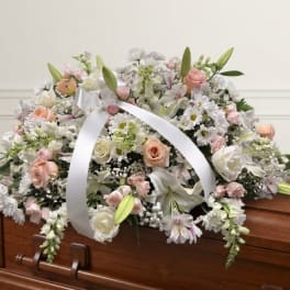 Pastel floral casket spray with white ribbon on a wooden coffin