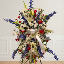Tall floral standing arrangement with red, white, and blue flowers and a white ribbon