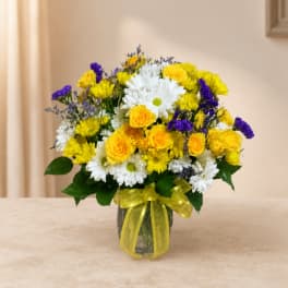 Bouquet of yellow, white, and purple flowers in a glass vase with a yellow ribbon