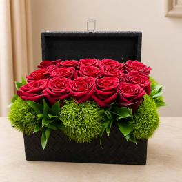 Red roses arranged in a black woven box with green accents