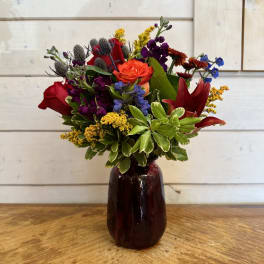 Mixed bouquet of red, orange, purple, and yellow flowers in a dark glass vase